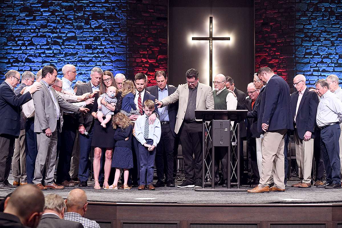 History_Thumb-06 Pastor Zac Hess installed. People on stage praying.